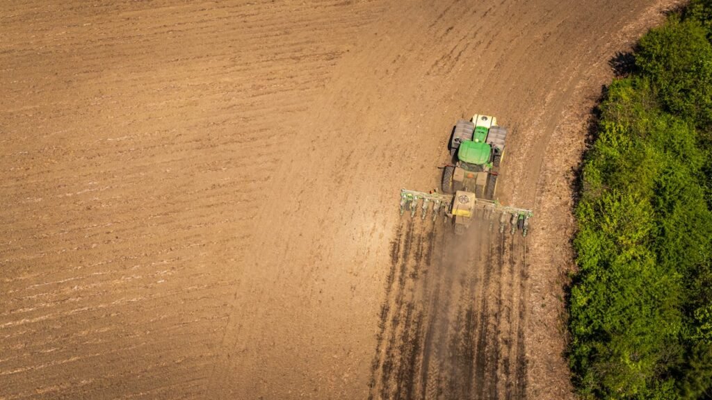 An aerial shot of a tractor plowing farmland, preparing soil for planting in summer.